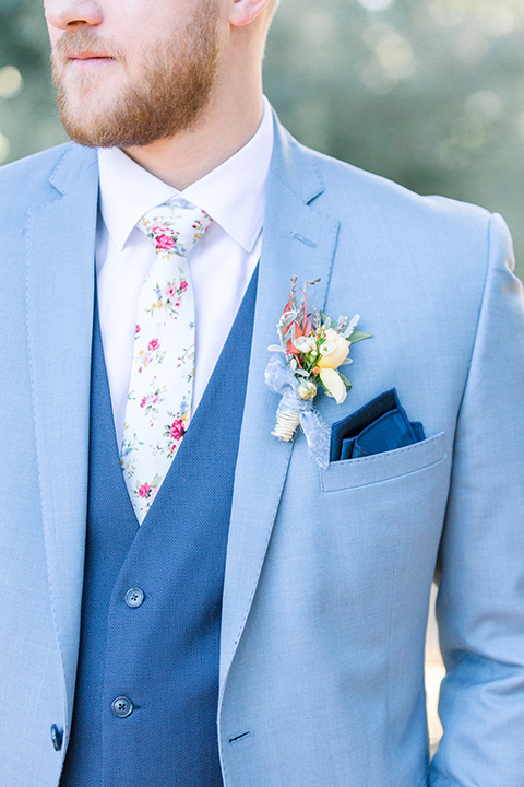 alice-in-wonderland-shoot-close-up-on-groom-attire-in-a-light-blue-coat-with-dark-blue-pants-and-a-floral-long-tie