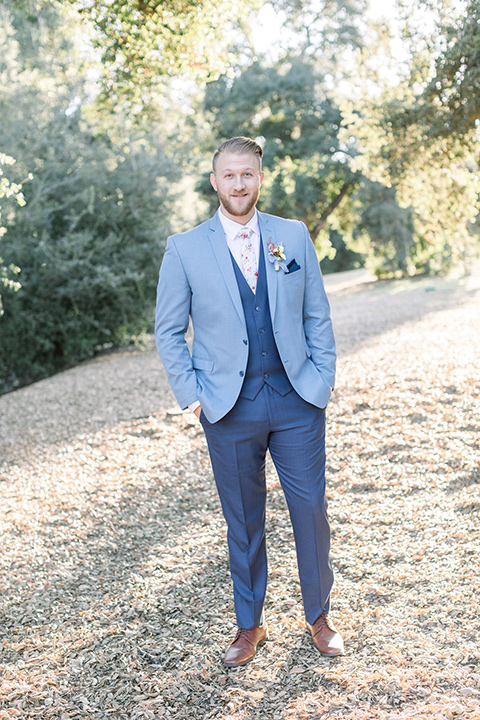 alice-in-wonderland-shoot-groom-looking-at-camera-in-a-light-blue-suit-with-dark-blue-pants-and-white-floral-long-tie