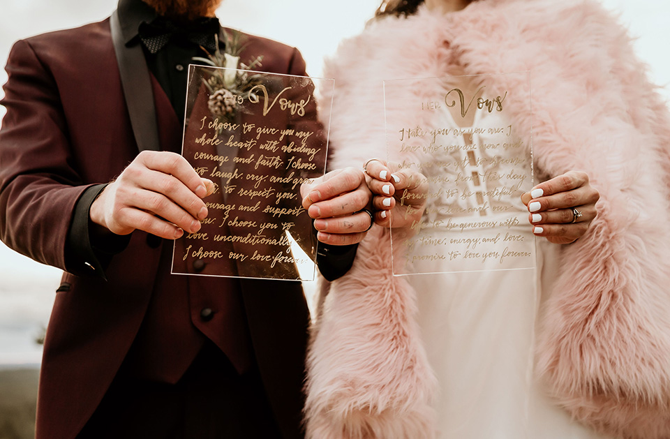 Arizona-Elopement-Shoot-close-up-on-invitations-the-bride-in-a-bohemian-white-gown-with-a-plunging-back-and-lace-detailing-the-groom-in-a-burgundy-shawl-lapel-tuxedo-with-a-black-shirt-and-bow-tie