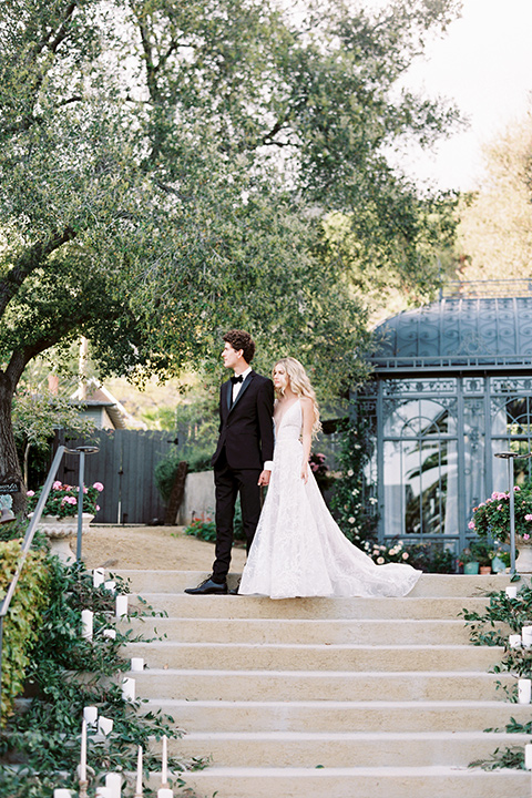 Artist-and-his-muse-shoot-bride-and-groom-walking-down-the-stairs-the-bride-in-a-white-ballgown-with-an-illusion-neckline-and-deep-v-neckline-and-the-groom-in-a-black-tuxedo-with-a-black-bow-tie