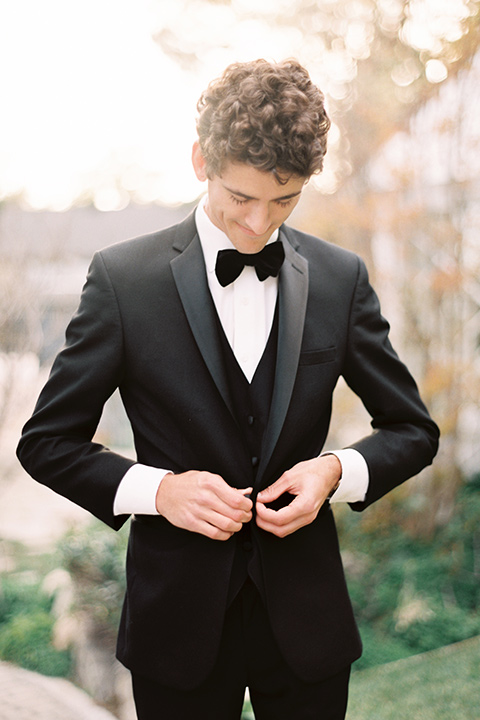 Artist-and-his-muse-shoot-groom-fixing-coat-in-a-black-tuxedo-with-a-black-bow-tie