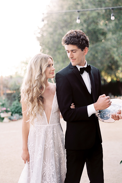 Artist-and-his-muse-shoot-groom-painting-looking-at-bride-the-bride-in-a-white-ball-gown-with-an-illusion-neckline-and-laace-detailing-and-the-groom-is-in-a-black-tuxedo-with-a-black-bow-tie