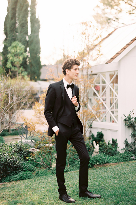 Artist-and-his-muse-shoot-groom-standing-in-a-black-tuxedo-with-a-black-bow-tie