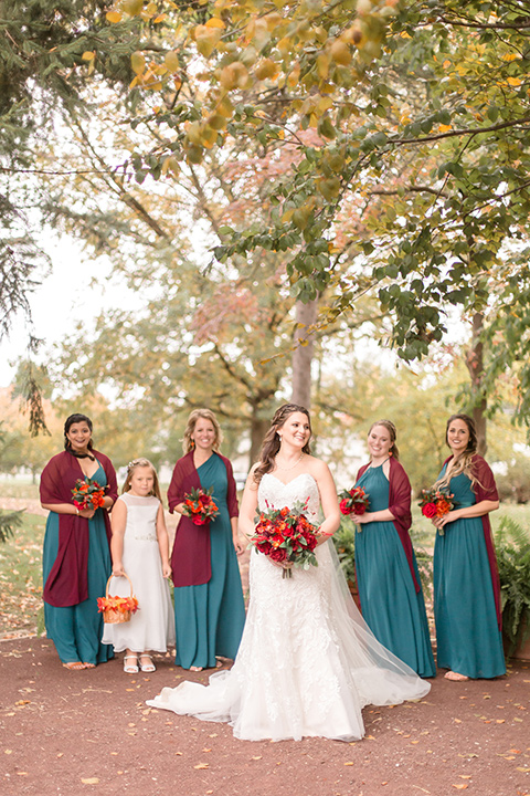  bride in an ivory lace gown with a long veil and train with her bridesmaids in teal and peacock colored gowns