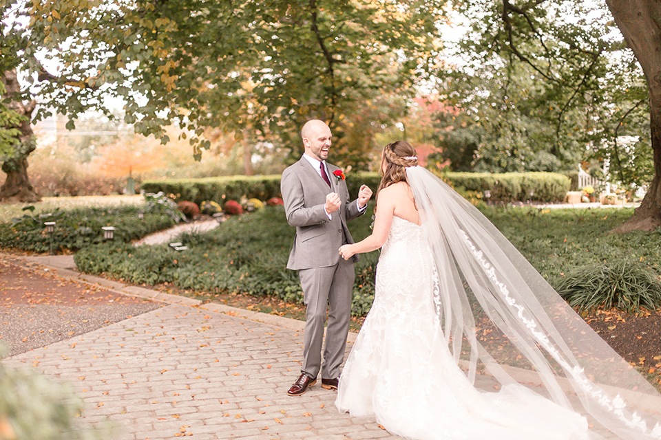 bride in an ivory lace gown with a long veil and train with the groom in a light brown suit with a red long tie and brown shoes, first look