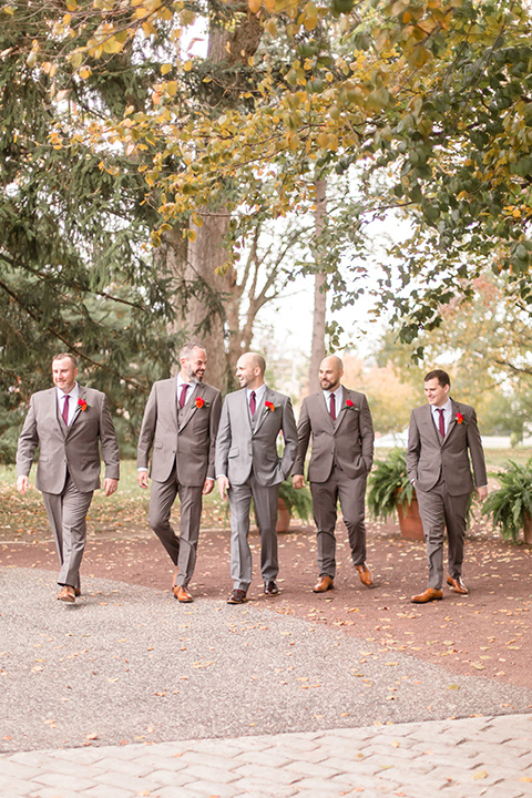  groom in a light brown suit with a red long tie and brown shoes, his groomsmen in a darker shade of brown suits with red ties