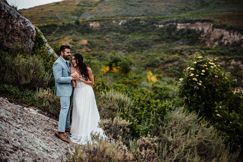 avila-beach-elopement-shoot-bride-and-groom-with-meadows-behind-them-bride-in-a-flowing-white-gown-with-a-soft-tulle-overlay-the-groom-wore-a-light-blue-suit-with-a-navy-long-tie