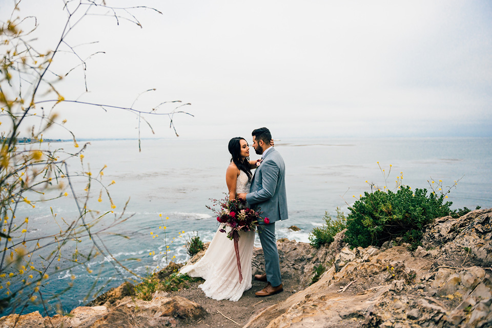 avila-beach-elopement-shoot-bride-and-groom-with-sweeping-views-behind-them-bride-in-a-flowing-white-gown-with-a-soft-tulle-overlay-the-groom-wore-a-light-blue-suit-with-a-navy-long-tie