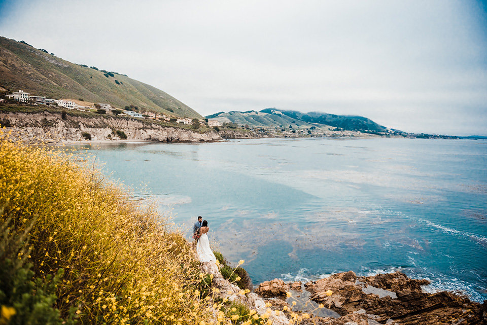 avila-beach-elopement-shoot-long-shot-of-bride-and-groom-bride-in-a-flowing-white-gown-with-a-soft-tulle-overlay-the-groom-wore-a-light-blue-suit-with-a-navy-long-tie