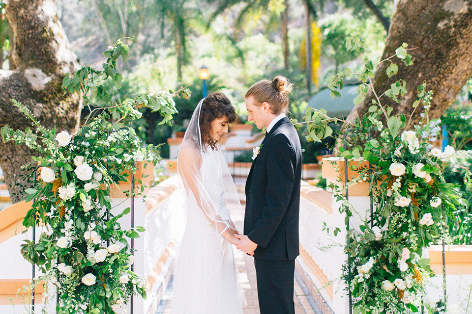 Rancho-las-lomas-blue-shoot-bride-and-groom-at-ceremony-looking-at-each-other-the-bride-wore-a-white-flowing-gown-with-a-halter-neckline-and-simple-mamkeup-the-groom-wore-a-simple-black-suit-with-a-black-long-tie