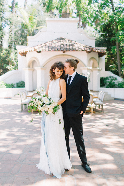 Rancho-las-lomas-blue-shoot-bride-and-groom-standing-smiling-the-bride-wore-a-white-dress-with-a-halter-neckline-and-black-notch-lapel-suit-and-black-long-tie