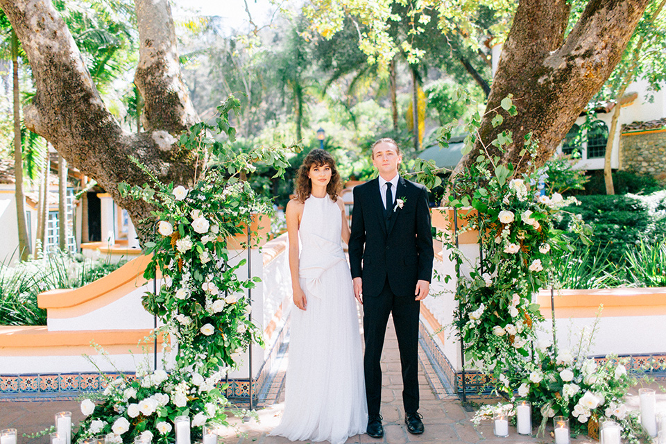 Rancho-las-lomas-blue-shoot-bride-and-groom-walking-away-from-ceremony-the-bride-wore-a-white-flowing-gown-with-a-halter-neckline-and-simple-mamkeup-the-groom-wore-a-simple-black-suit-with-a-black-long-tie