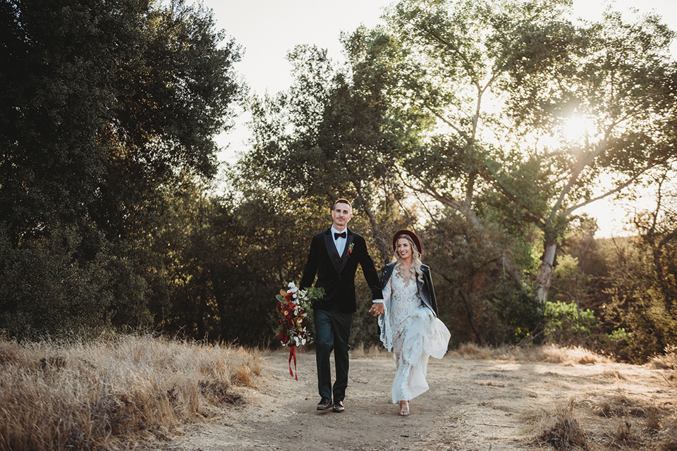 owl-creek-farms-bride-and-groom-walking-bride-wearing-a-boho-lace-long-sleeved-gown-with-a-high-neckline-groom-wears-a-black-velvet-coat-with-grey-pants-and-a-black-bow-tie