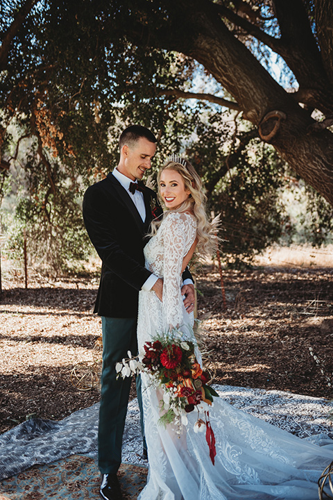 owl-creek-farms-bide-and-groom-touching-heads-owl-creek-farms-bide-and-groom-touching-heads-bride-wearing-a-boho-style-dress-with-long-sleeves-and-a-high-neckline-with-a-burgundy-wide-brimmed-hat-groom-wearing-a-velvet-tuxedo-with-grey-pants