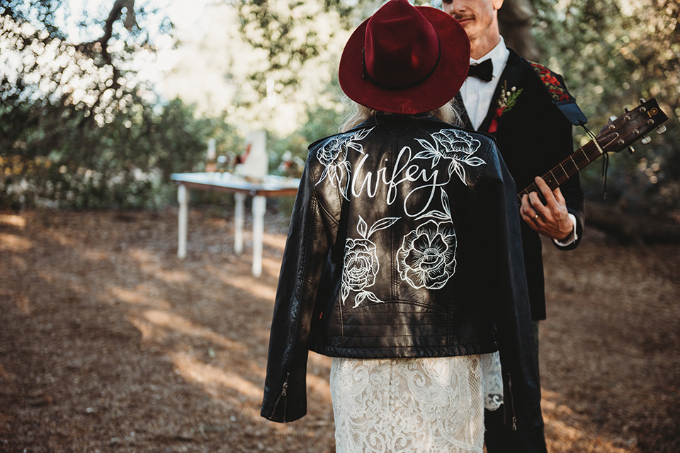 owl-creek-farms-leather-jacket-with-lettering-bride-wearing-a-boho-lace-long-sleeved-gown-with-a-high-neckline-and-leather-jacket-groom-wears-a-black-velvet-coat-with-grey-pants-and-a-black-bow-tie