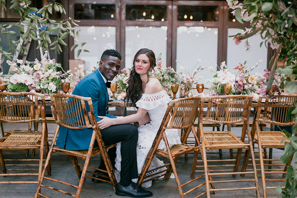 Brooklyn-Shoot-bride-and-groom-sitting-at-the-tables-groom-in-a-teal-coat-with-black-pants-and-a-black-bow-tie-the-bride-wears-a-bohemian-style-gown-with-flutter-sleeves-and-loose-hair