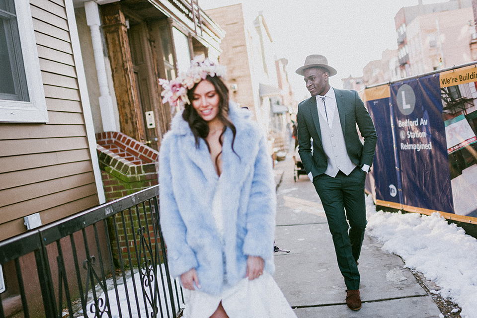 Brooklyn-Shoot-bride-and-groom-walking-and-smiling-groom-in-a-green-suit-with-a-bolo-tie-the-bride-wears-a-bohemian-style-gown-with-flutter-sleeves-and-loose-hair-and-a-blue-faux-fur-coat