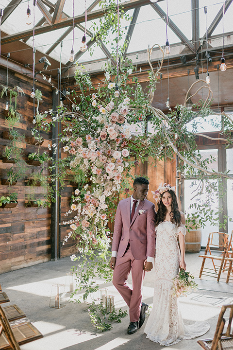 Brooklyn-Shoot-bride-and-groom-walking-in-ceremony-space-bride-in-a-lace-boho-gown-with-an-off-the-shoulder-detail-groom-in-a-rose-pink-suit-with-brown-shoes-and-a-burgundy-tie