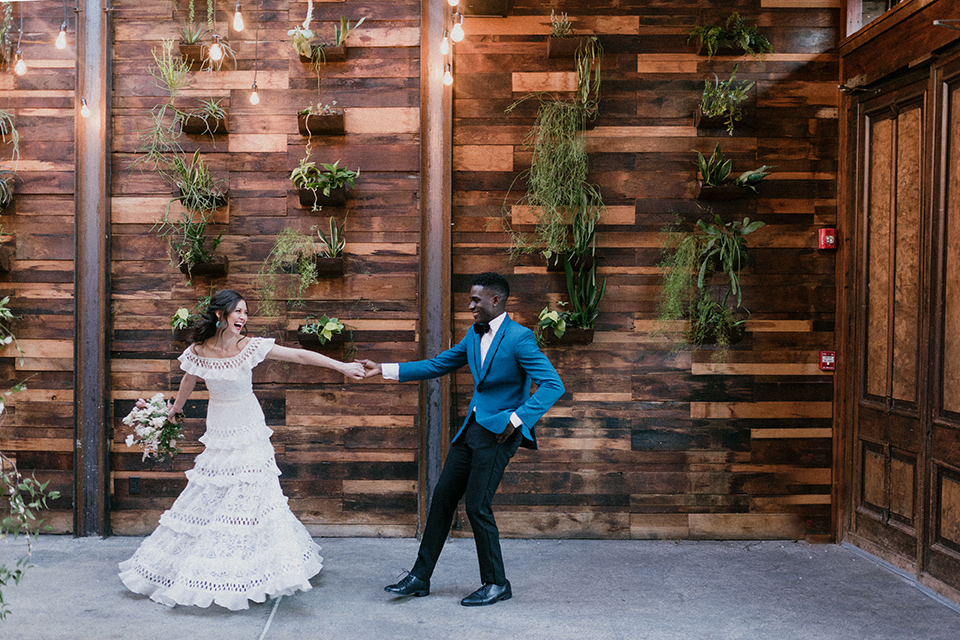 Brooklyn-Shoot-bride-and-groom-walking-groom-in-a-teal-coat-with-black-pants-and-a-black-bow-tie-the-bride-wears-a-bohemian-style-gown-with-flutter-sleeves-and-loose-hair
