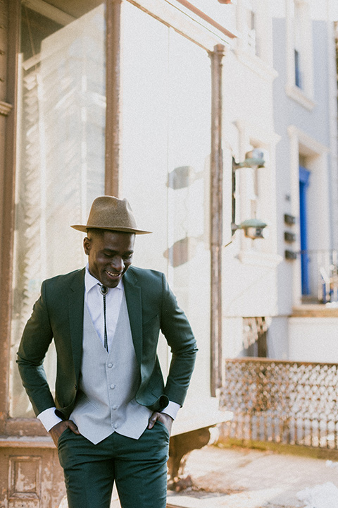 Brooklyn-Shoot-groom-smiling-looking-down-in-a-green-suit-with-a-grey-vest-and-bolo-tie