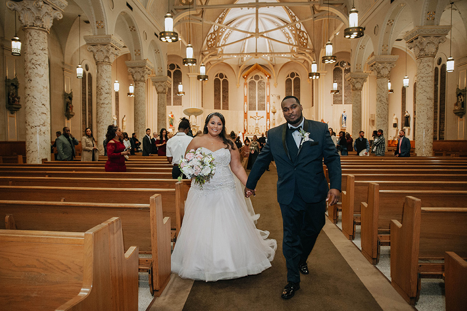 Fete-Venue-New-Orleans-Wedding-bride-and-groom-walking-down-aisle-bride-in-a-tulle-strapless-ballgown-groom-in-a-navy-blue-tuxedo