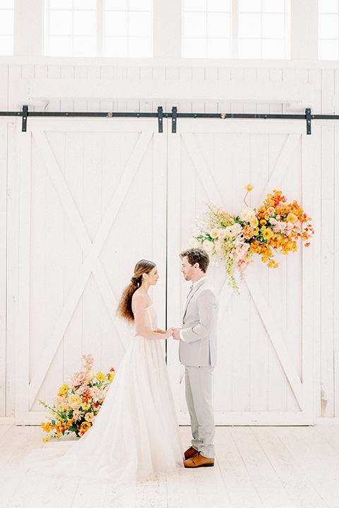 bride and groom at ceremony, bride in a full tulle ballgown with a strapless design and the groom in a light grey suit with pink bow tie