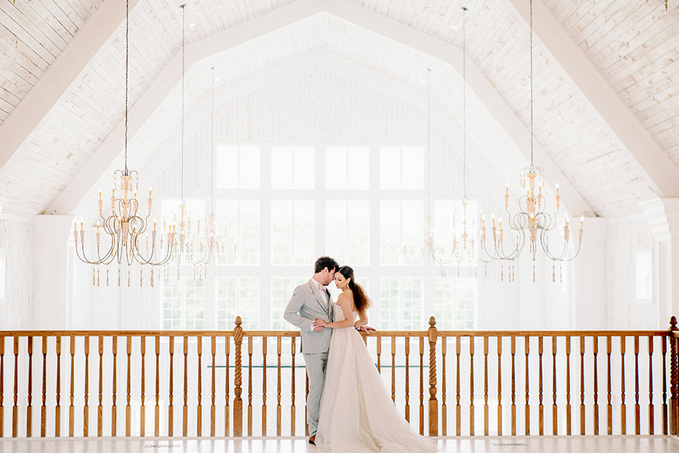 bride and groom standing on the loft, bride in a full tulle ballgown with a strapless design and the groom in a light grey suit with pink bow tie