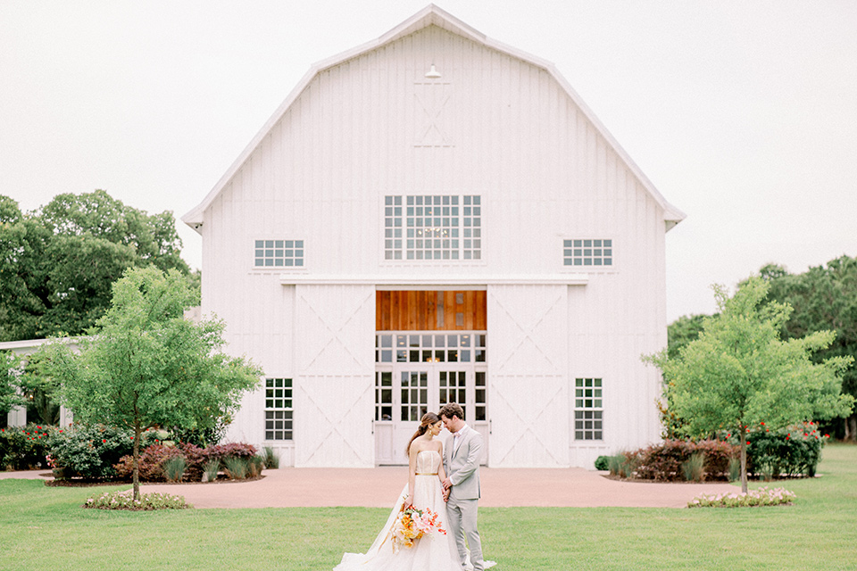 bride and groom outside the barn, bride in a full tulle ballgown with a strapless design and the groom in a light grey suit with pink bow tie