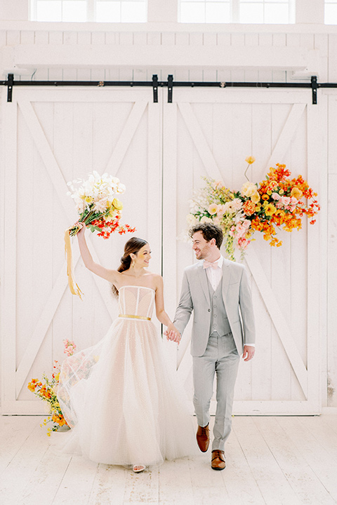 bride and groom leaving ceremony, bride in a full tulle ballgown with a strapless design and the groom in a light grey suit with pink bow tie