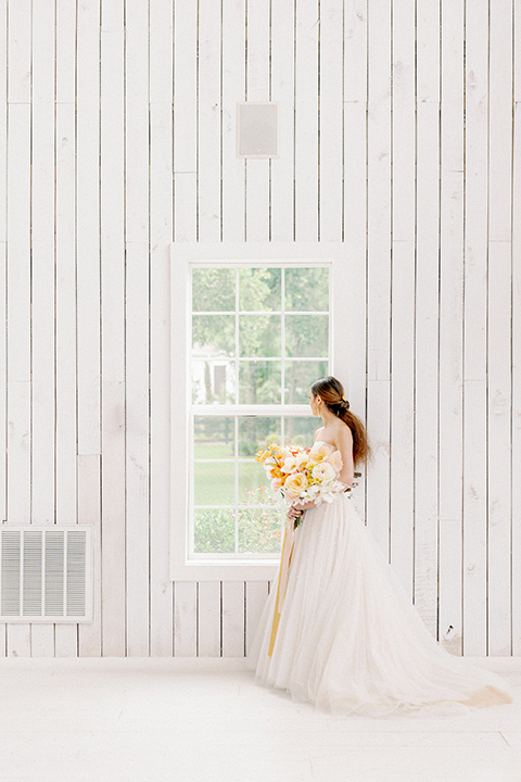  bride in a full tulle ballgown with a strapless design holding colorful golden toned flowers