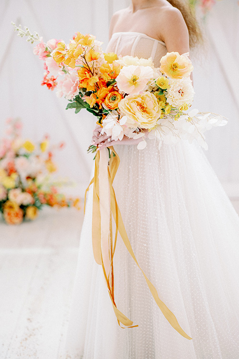 bride in a full tulle ballgown with a strapless design holding gold and orange flowers