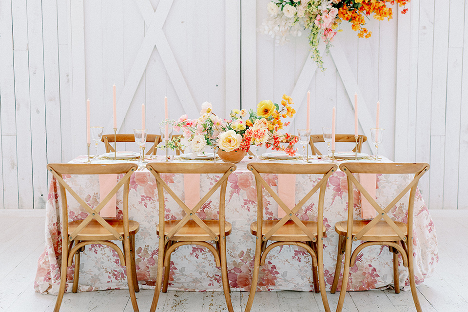 pink and white floral linen with gold charger plates and flatware and wooden chairs