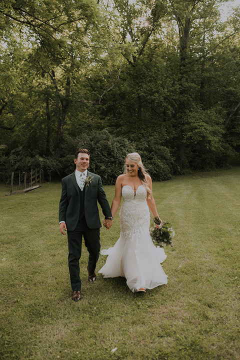 Horse-Range-Vista-bride-and-groom-walking-towards-camera-bride-in-a-lace-strapless-mermaid-gown-and-groom-in-a-green-suit-with-floral-tie