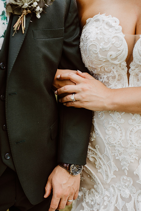 Horse-Range-Vista-close-up-on-couples-attire-bride-in-a-lace-mermaid-gown-with-a-sweetheart-neckline-groom-in-a-green-suit-with-a-floral-tie