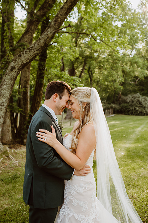 Horse-Range-Vista-couple-touching-heads-bride-in-a-lace-strapless-mermaid-gown-and-groom-in-a-green-suit-with-floral-tie