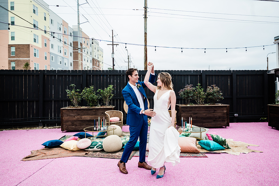 bride and groom dancing, bride is in a formfitting gown with straps and her hair down in a loose style while the groom is in a cobalt blue suit with brown shoes and his shirt undone