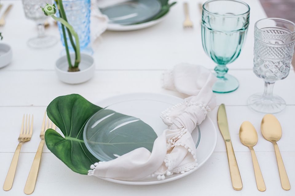 table flatware in gold with a white linen and a palm leaf as decor