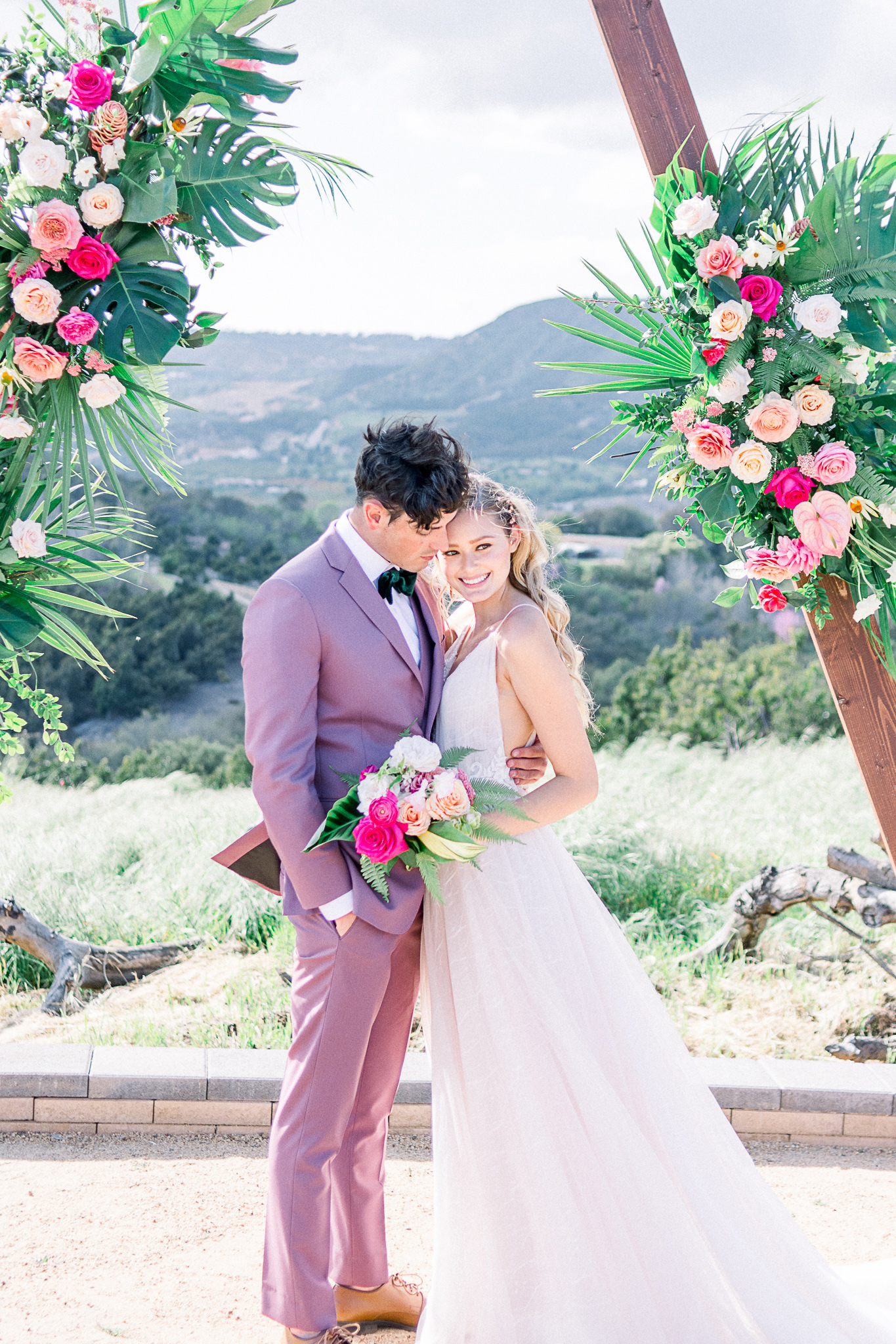 emerald-peak-temecula-wedding-bride-and-groom-ceremony-bride-in-a-blush-tulle-gown-with-straps-groom-in-a-rose-pink-suit-with-a-green-velvet-bow-tie