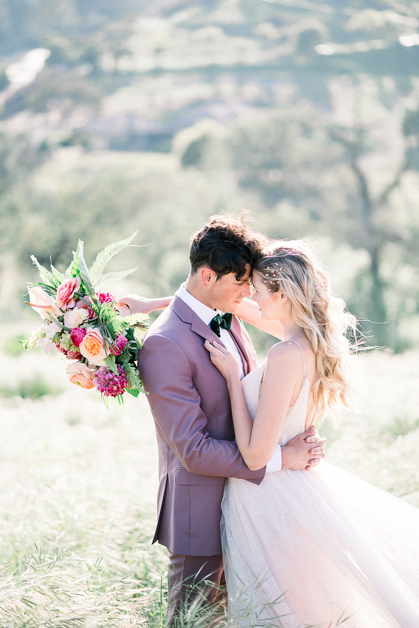 emerald-peak-temecula-wedding-bride-and-groom-touching-heads-bride-in-a-blush-tulle-gown-with-straps-groom-in-a-rose-pink-suit-with-a-green-velvet-bow-tie