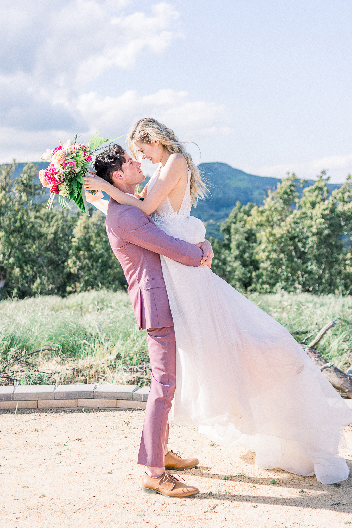 emerald-peak-temecula-wedding-groom-holding-up-bride-bride-in-a-blush-toned-tulle-ballgown-with-straps-groom-in-a-rose-pink-suit-with-a-green-velvet-bow-tie