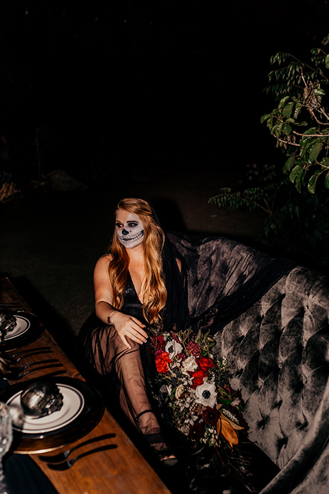 bride in a black gown with a black train and groom in a burgundy tuxedo with a black shirt both with their face painted in a skull pattern