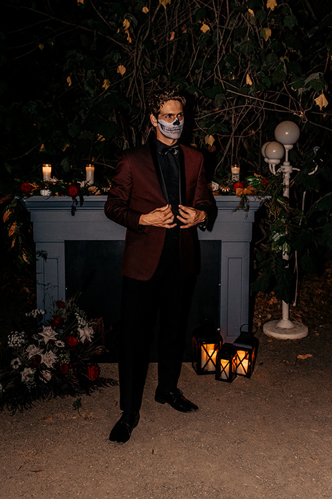  bride in a black gown with a black train and groom in a burgundy tuxedo with a black shirt both with their face painted in a skull pattern 