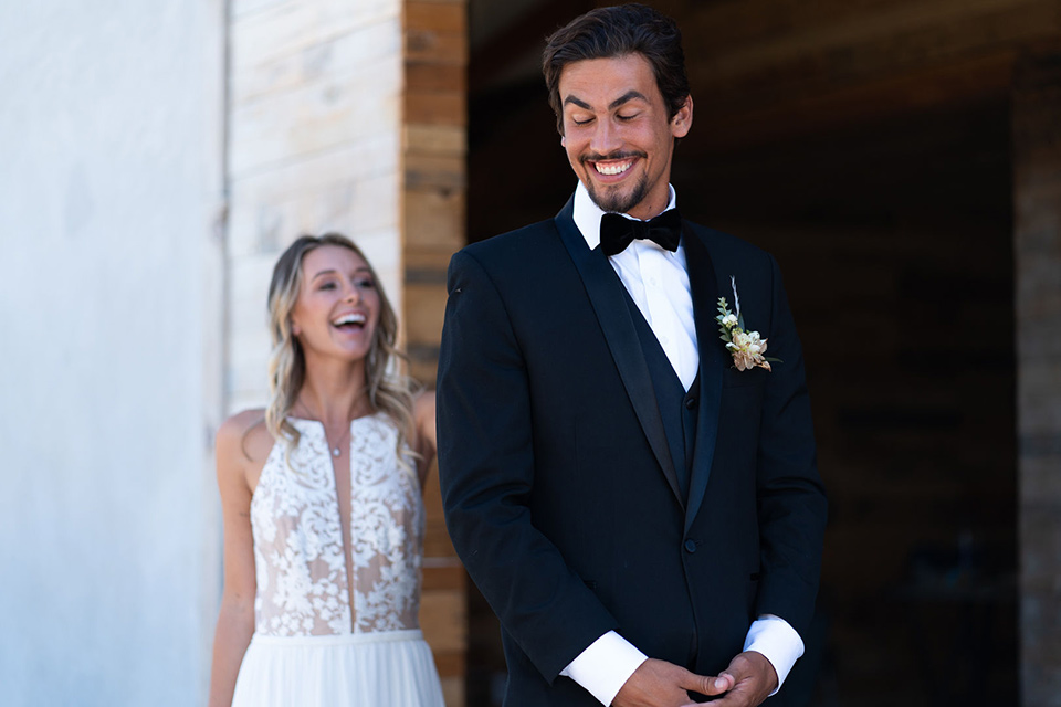 la-bonita-ranch-rustic-shoot-bride-and-groom-first-look-the-bride-in-a-white-bohemian-gown-with-a-nude-underlay-and-lace-detailing-groom-in-a-navy-shawl-lapel-tuxedo-with-a-black-bow-tie