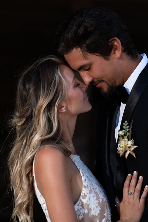 la-bonita-ranch-rustic-shoot-bride-and-groom-touching-heads-bridal-gown-with-a-high-neckline-and-a-nude-underlay-groom-in-a-navy-shawl-lapel-tuxedo-with-a-black-bowtie