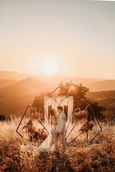 bride in a white bohemian style lace gown with a straps and a her hair in loose waves and the groom in a light grey suit