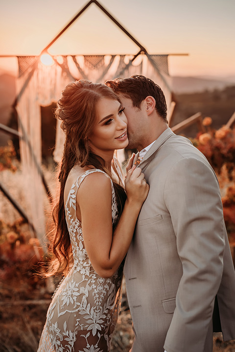  bride in a white bohemian style lace gown with a straps and a her hair in loose waves with the groom in a light grey suit