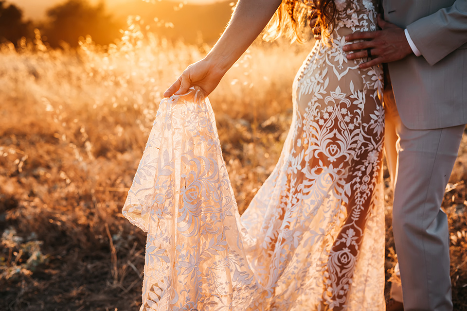  bride in a white bohemian style lace gown with a straps and a her hair in loose waves with the groom in a light grey suit