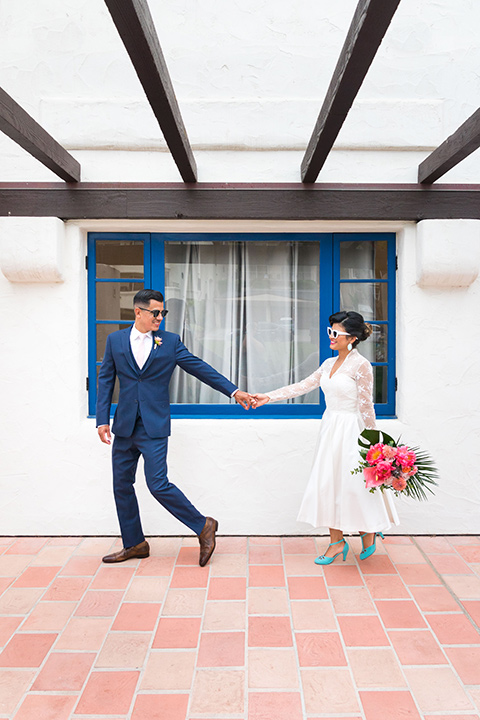 Ole-Hanson-Beach-Club-bride-and-groom-walking-the-bride-wore-a-tea-length-gown-with-lace-sleeves-and-teal-retro-inspired-heels-the-groom-wore-a-dark-blue-suit-with-a-light-pink-long-tie-and-brown-shoes