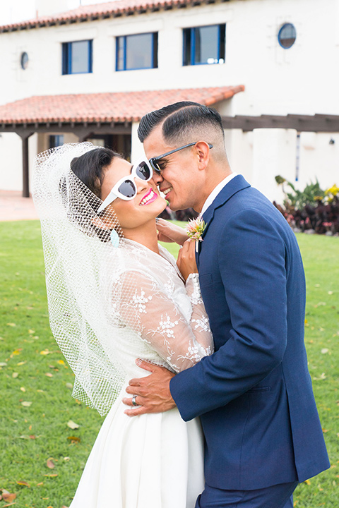 Ole-Hanson-Beach-Club-bride-and-groom-with-sunglasses-the-bride-wore-a-tea-length-retro-inspired-gown-with-lace-sleeves-and-an-elbow-length-veil-and-teal-blue-heels-the-groom-wore-a-dark-blue-suit-with-a-light-pink-long-tie-and-brown-shoes