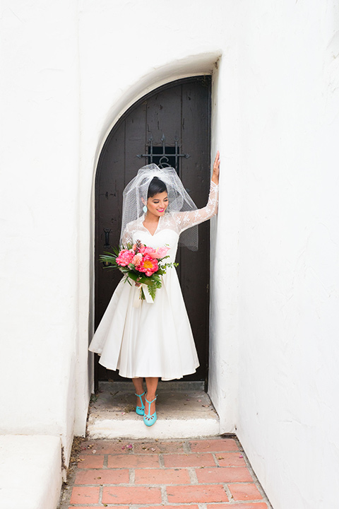 Ole-Hanson-Beach-Club-bride-looking-at-the-camera-in-a-tea-length-retro-inspired-gown-with-lace-sleeves-and-an-elbow-length-veil-and-teal-blue